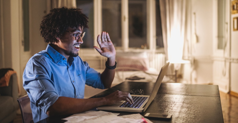 photo of a man waving at the screen of his laptop