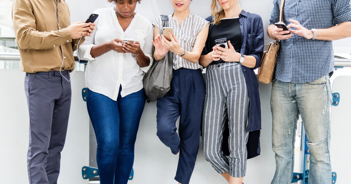 five people leaning against a wall looking down at their phones