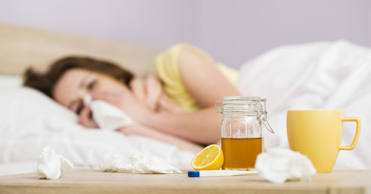 photo of a sick woman laying in bed blowing her nose