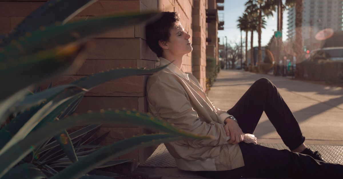 photo of a person with closed eyes sitting on the ground leaning against a wall